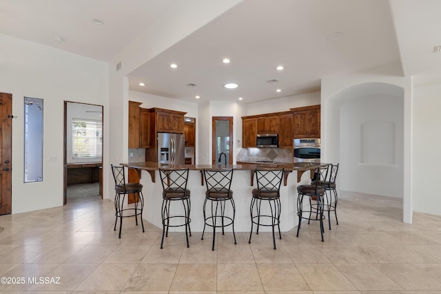 kitchen with decorative backsplash, a breakfast bar area, dark countertops, a sink, and stainless steel appliances