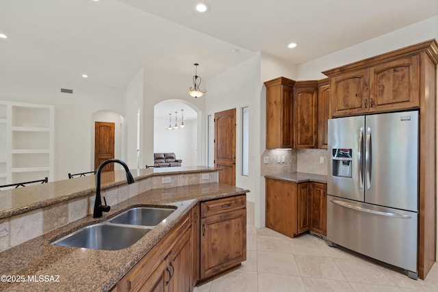 kitchen featuring stainless steel fridge, a sink, arched walkways, dark stone countertops, and light tile patterned floors