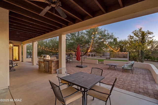 patio terrace at dusk featuring a ceiling fan, outdoor dining area, exterior kitchen, and area for grilling