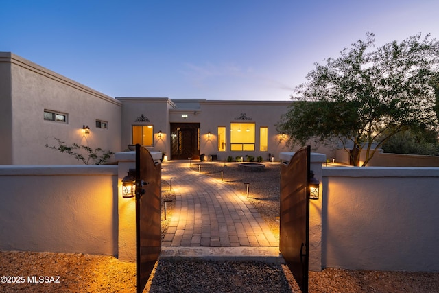 adobe home with a gate, stucco siding, a fire pit, and a fenced front yard