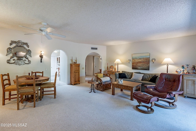 living area with light colored carpet, arched walkways, a textured ceiling, and ceiling fan