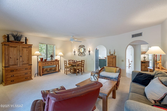 living area with light colored carpet, arched walkways, a textured ceiling, a ceiling fan, and visible vents