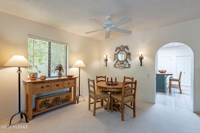 dining space featuring carpet flooring, arched walkways, ceiling fan, and a textured ceiling
