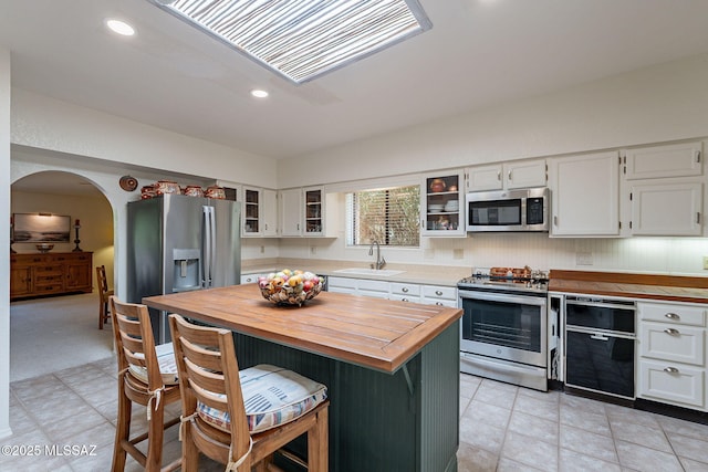 kitchen with appliances with stainless steel finishes, a sink, butcher block countertops, a center island, and white cabinetry