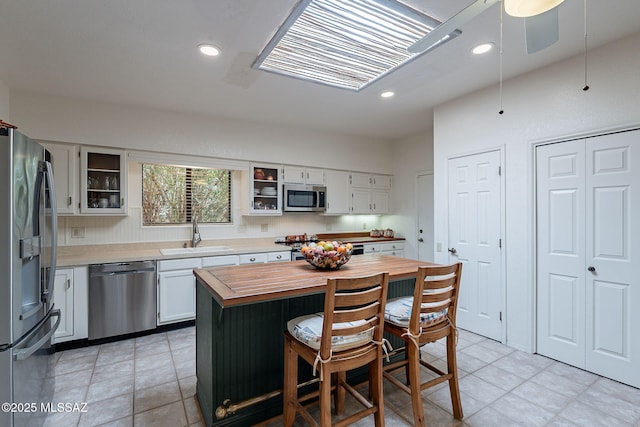 kitchen with a kitchen island, butcher block countertops, white cabinetry, a sink, and stainless steel appliances