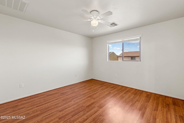 empty room with wood finished floors, visible vents, a ceiling fan, and baseboards