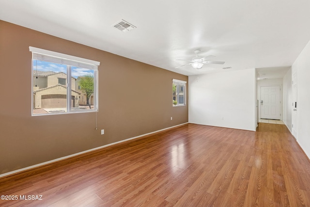 empty room featuring light wood-style flooring, visible vents, a ceiling fan, and baseboards