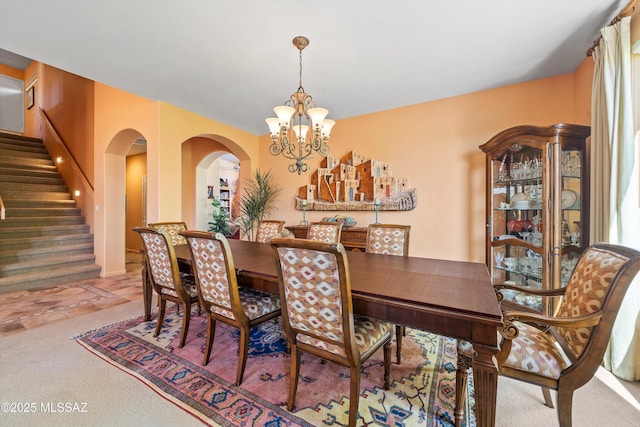 carpeted dining area with arched walkways, a chandelier, and stairway