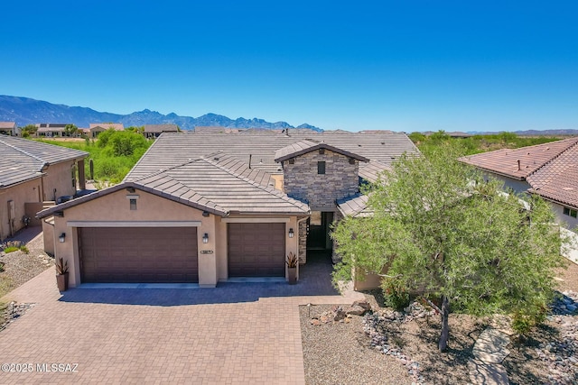 ranch-style house featuring a mountain view, a tile roof, a garage, stucco siding, and decorative driveway