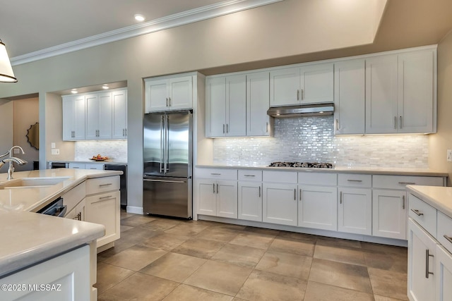 kitchen with under cabinet range hood, a sink, crown molding, light countertops, and appliances with stainless steel finishes