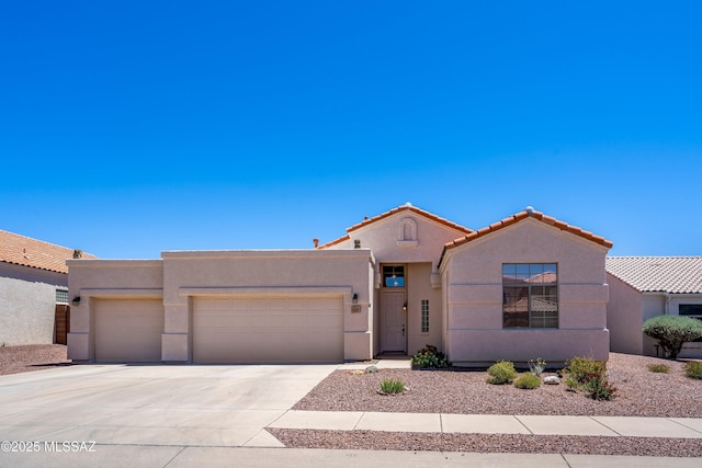 view of front of property featuring stucco siding, driveway, a tile roof, and a garage