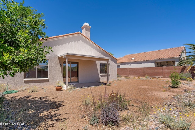 back of house with fence, stucco siding, a chimney, a patio area, and a tiled roof