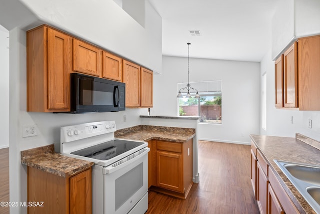 kitchen featuring black microwave, a peninsula, wood finished floors, and electric stove