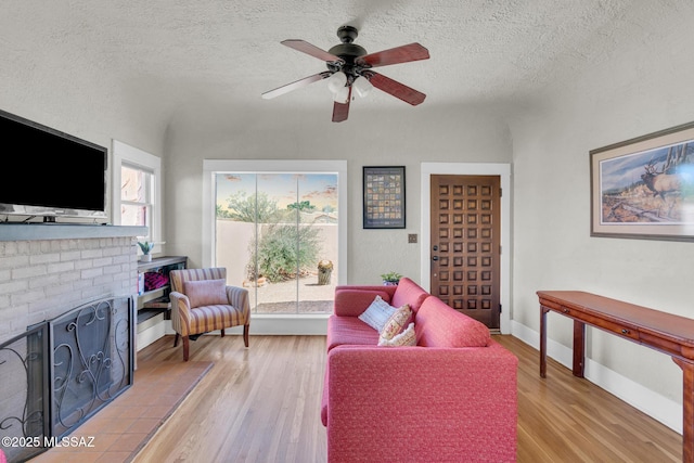 2716 E 6th St, Tucson, AZ 85716 - living room with light wood-style floors, ceiling fan, a textured ceiling, baseboards, and a brick fireplace