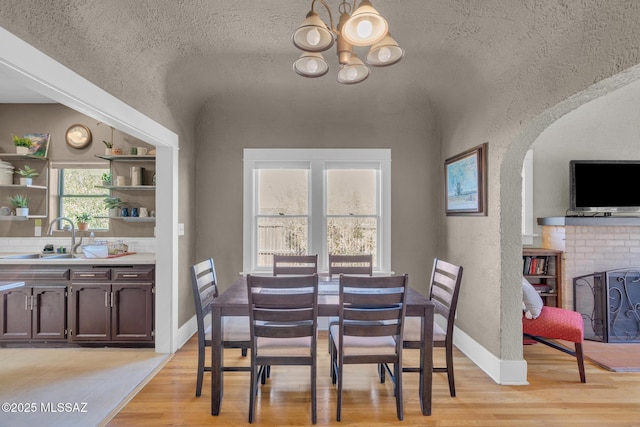 2716 E 6th St, Tucson, AZ 85716 - dining space featuring a chandelier, light wood finished floors, arched walkways, a textured wall, and vaulted ceiling