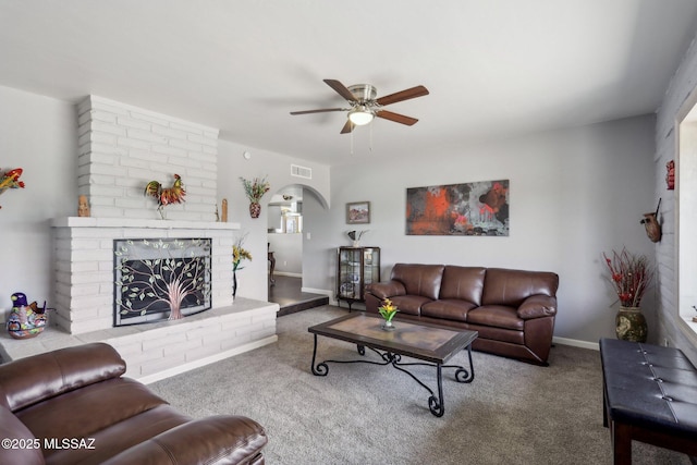 carpeted living area with ceiling fan, a brick fireplace, arched walkways, baseboards, and visible vents