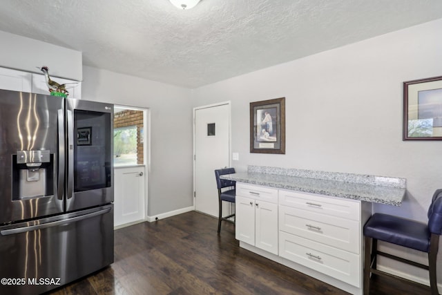 kitchen featuring stainless steel fridge, white cabinets, a breakfast bar area, and light stone countertops