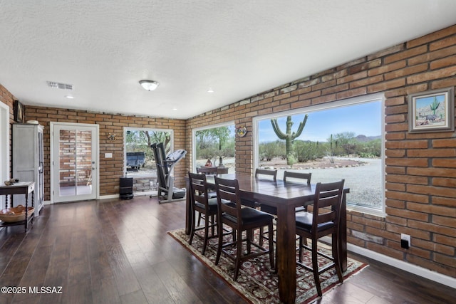 dining room with a textured ceiling, dark wood finished floors, brick wall, and a wealth of natural light