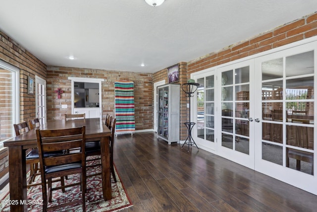 dining space with brick wall, plenty of natural light, french doors, and wood finished floors