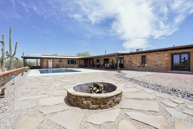 rear view of house with a patio, a fire pit, an outdoor pool, and brick siding