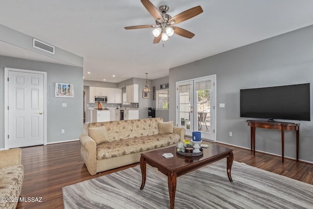 living area featuring dark wood-type flooring, visible vents, ceiling fan, and baseboards
