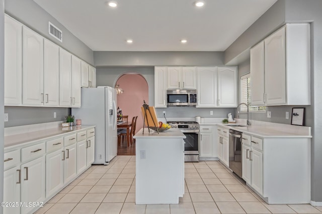 kitchen with arched walkways, appliances with stainless steel finishes, a center island, a sink, and visible vents