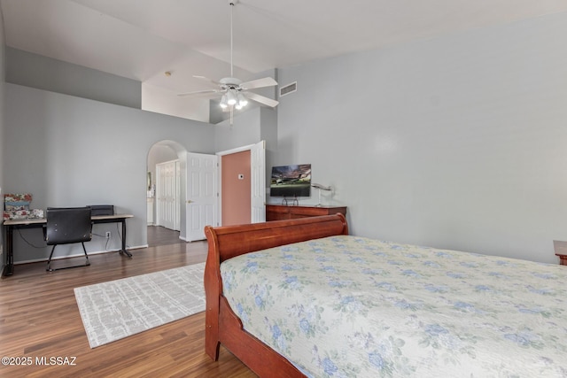 bedroom featuring visible vents, arched walkways, wood finished floors, a ceiling fan, and high vaulted ceiling