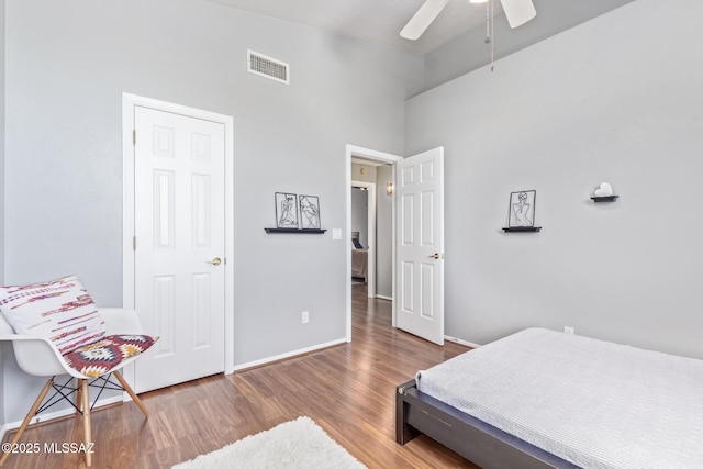 bedroom with visible vents, ceiling fan, baseboards, wood finished floors, and a high ceiling