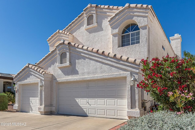view of front facade with stucco siding, a tiled roof, concrete driveway, and an attached garage