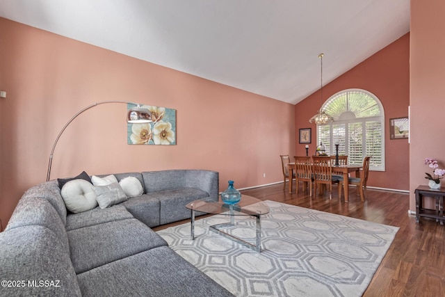 living area with wood finished floors, a chandelier, high vaulted ceiling, and baseboards