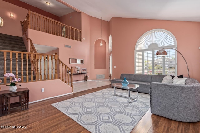 living area featuring wood finished floors, stairs, baseboards, visible vents, and high vaulted ceiling