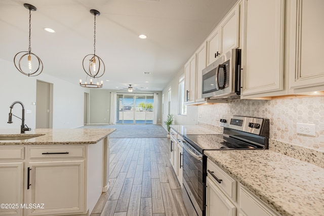 kitchen with a sink, light wood-style floors, ceiling fan with notable chandelier, stainless steel appliances, and backsplash