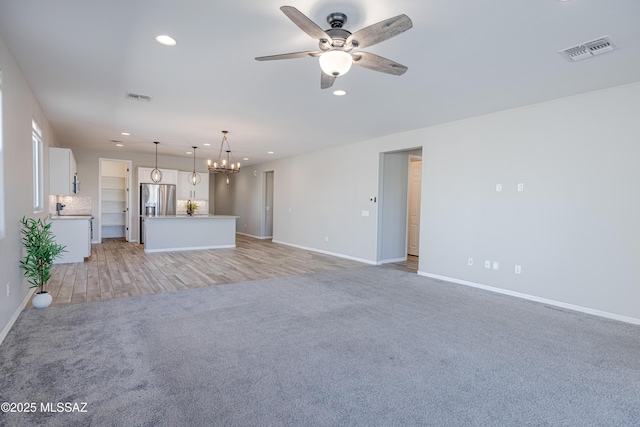 unfurnished living room featuring light colored carpet, visible vents, recessed lighting, and ceiling fan with notable chandelier