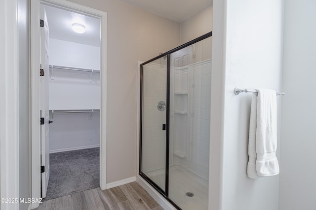 full bath featuring baseboards, a walk in closet, a shower stall, and wood finished floors