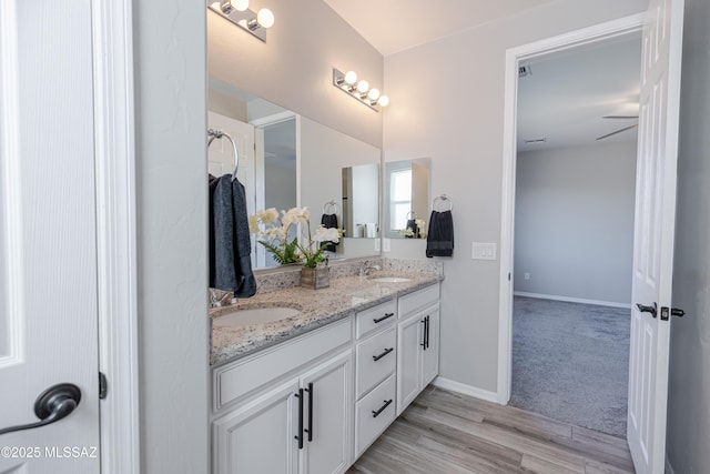 bathroom with double vanity, a sink, baseboards, and wood finished floors