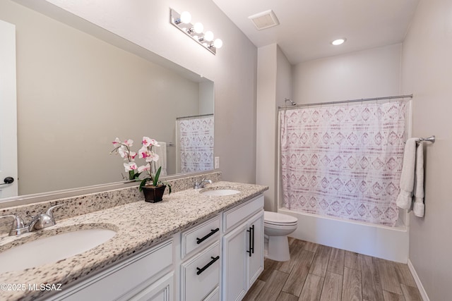 full bath featuring double vanity, toilet, a sink, and wood finished floors