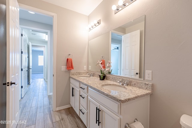 bathroom featuring double vanity, toilet, a sink, and wood finished floors