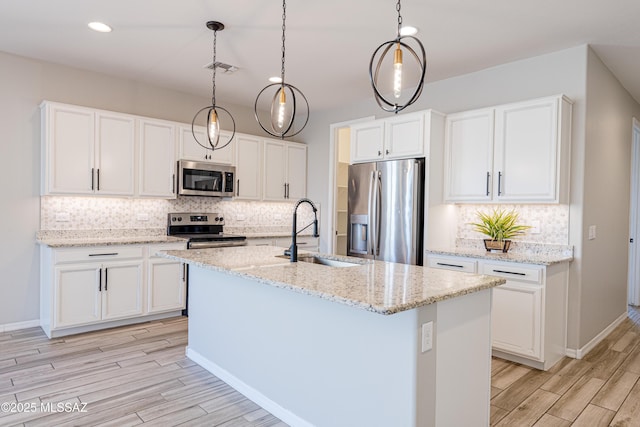 kitchen with backsplash, appliances with stainless steel finishes, a sink, white cabinets, and light wood-style flooring