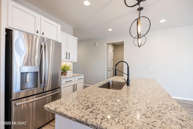 kitchen with light stone countertops, light wood-style floors, stainless steel fridge, white cabinets, and a sink