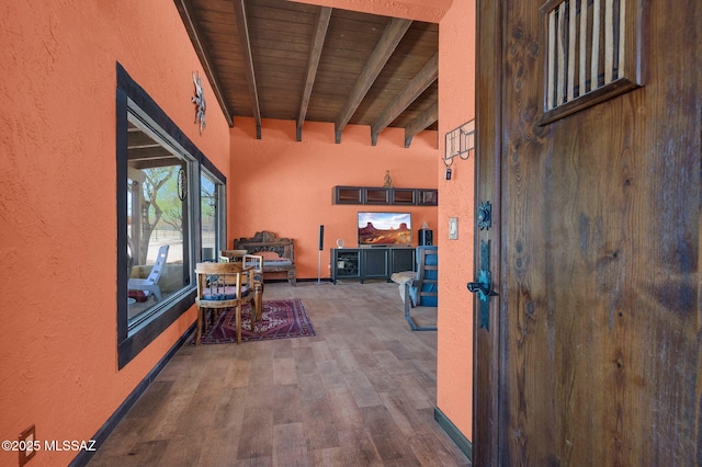 interior space with beamed ceiling, a high ceiling, wooden ceiling, a textured wall, and wood finished floors