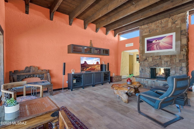 living room featuring wooden ceiling, an outdoor stone fireplace, beam ceiling, visible vents, and wood finished floors