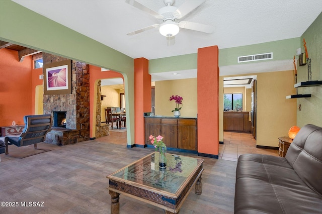 living room featuring arched walkways, wood finished floors, ceiling fan, a fireplace, and visible vents