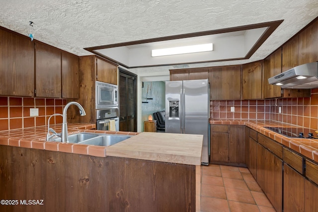 kitchen with decorative backsplash, a sink, appliances with stainless steel finishes, tile counters, and under cabinet range hood