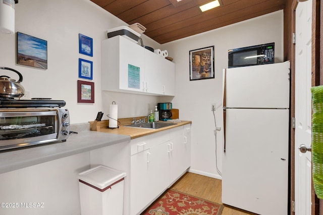 kitchen featuring white cabinets, a sink, black microwave, freestanding refrigerator, and wooden ceiling