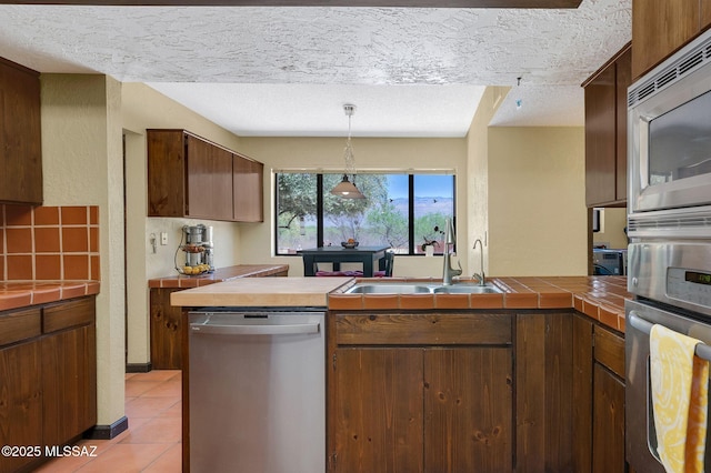 kitchen with a sink, tile counters, a peninsula, a textured ceiling, and appliances with stainless steel finishes