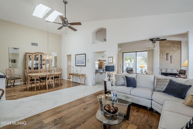 living area with visible vents, a skylight, wood finished floors, high vaulted ceiling, and ceiling fan with notable chandelier