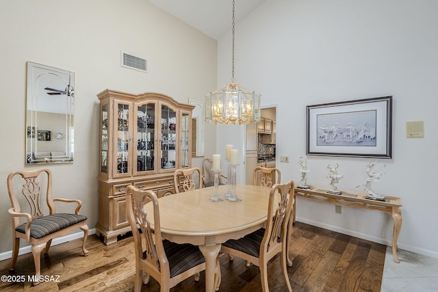 dining space with light wood-style floors, high vaulted ceiling, a chandelier, baseboards, and visible vents