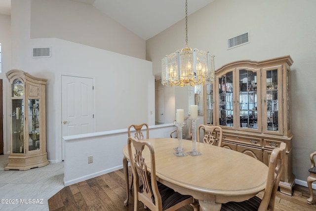 dining space featuring an inviting chandelier, light wood-style floors, visible vents, and high vaulted ceiling