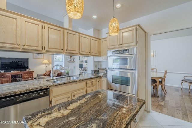 kitchen with a sink, appliances with stainless steel finishes, light brown cabinets, and dark stone countertops
