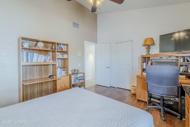 bedroom featuring ceiling fan, wood finished floors, a towering ceiling, visible vents, and a closet